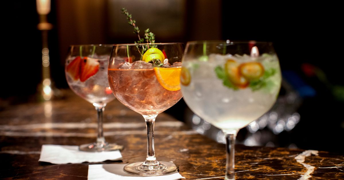 Three fruit-garnished gin and tonic cocktails in balloon glasses on a dark marble bar top.