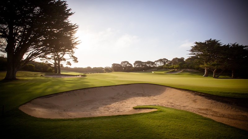 Scenic golf course with sand bunker, manicured green fairway, and tall trees at dusk