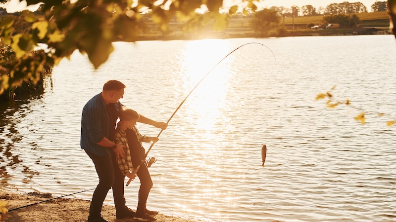 Father and child fishing together along a lake shore at golden hour