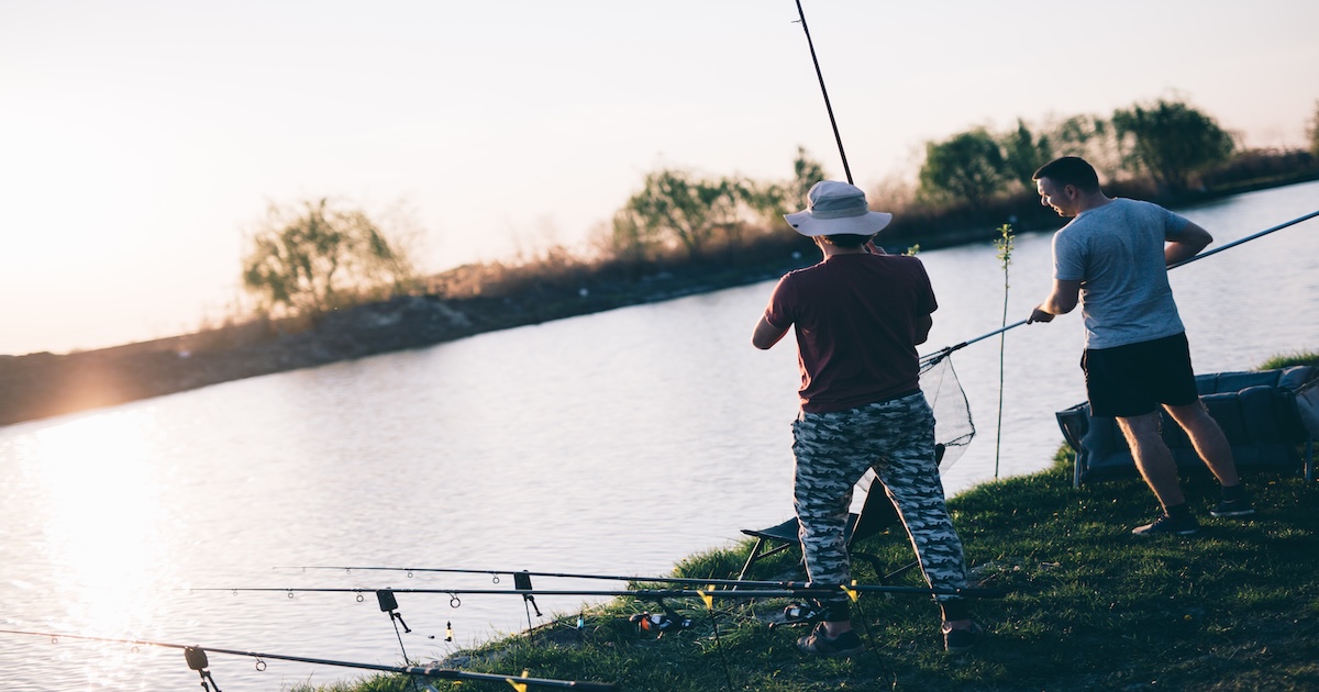 Two men fishing at a calm lake during a golden sunset