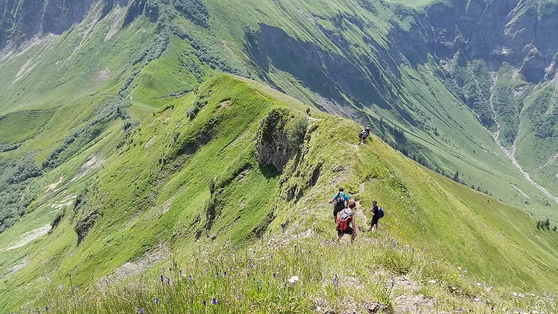 Hikers walking along a green mountain ridge trail with panoramic views