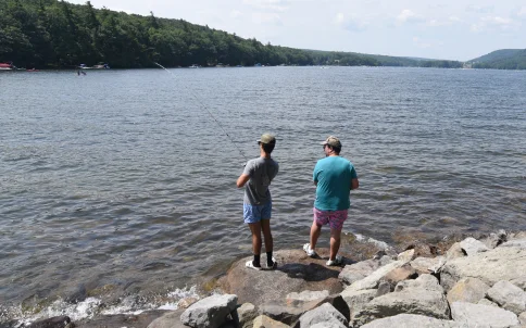 Two anglers fishing from rocks along the lake shore