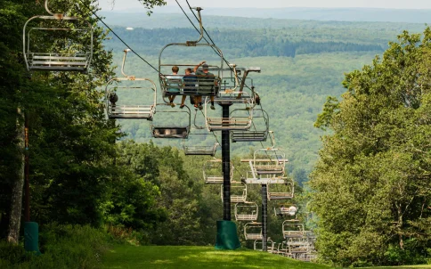 Chairlift riders overlooking green mountains at Wisp Resort