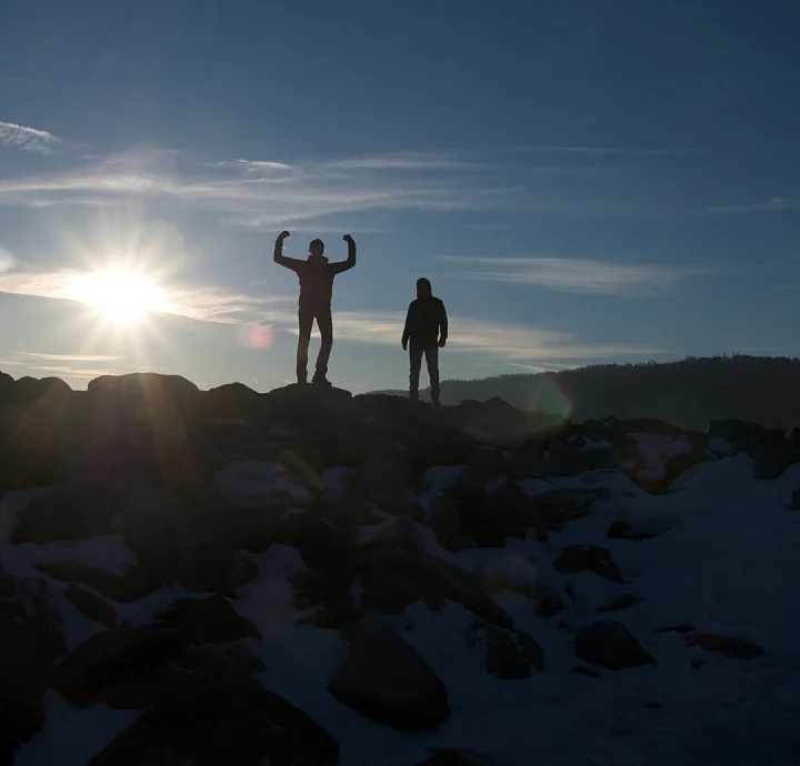 Two hikers standing on a rocky overlook at sunrise
