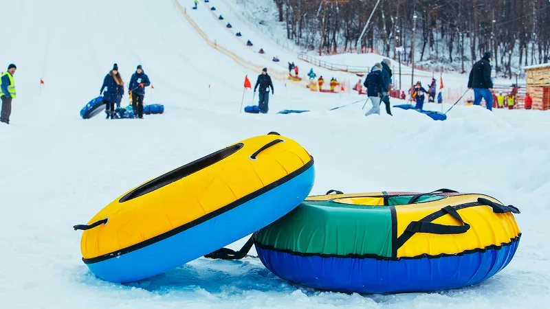 Two colorful snow tubes on a slope with tubers walking up the hill behind them