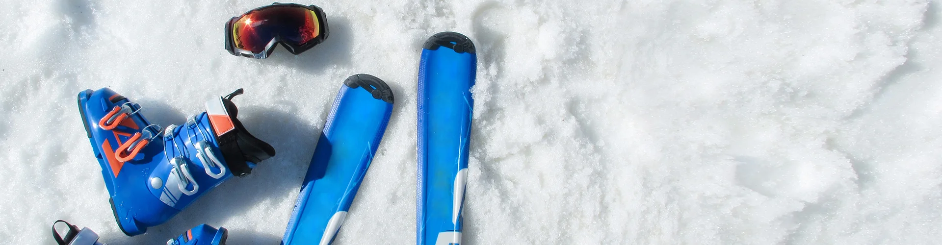 Blue ski boots, skis, and goggles resting on snow